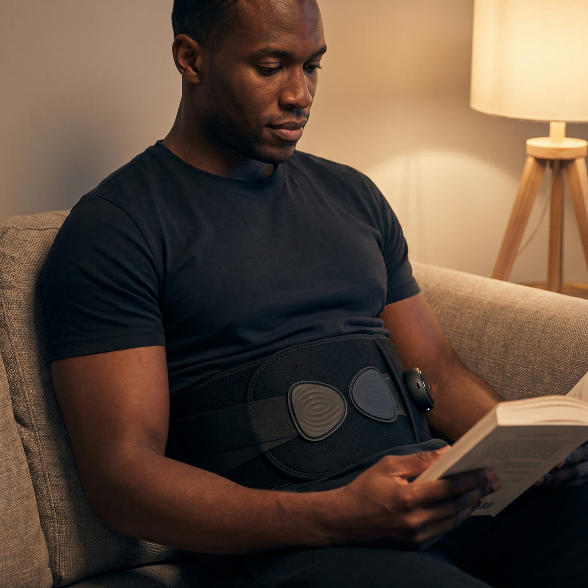 A man reading on a couch wearing the Unknot Heat Belt