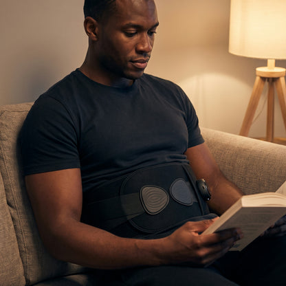 A man reading on a couch wearing the Unknot Heat Belt