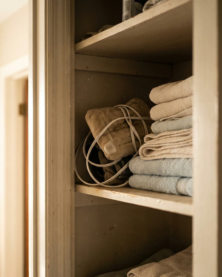 A corded heating pad coiled on a shelf in a closet